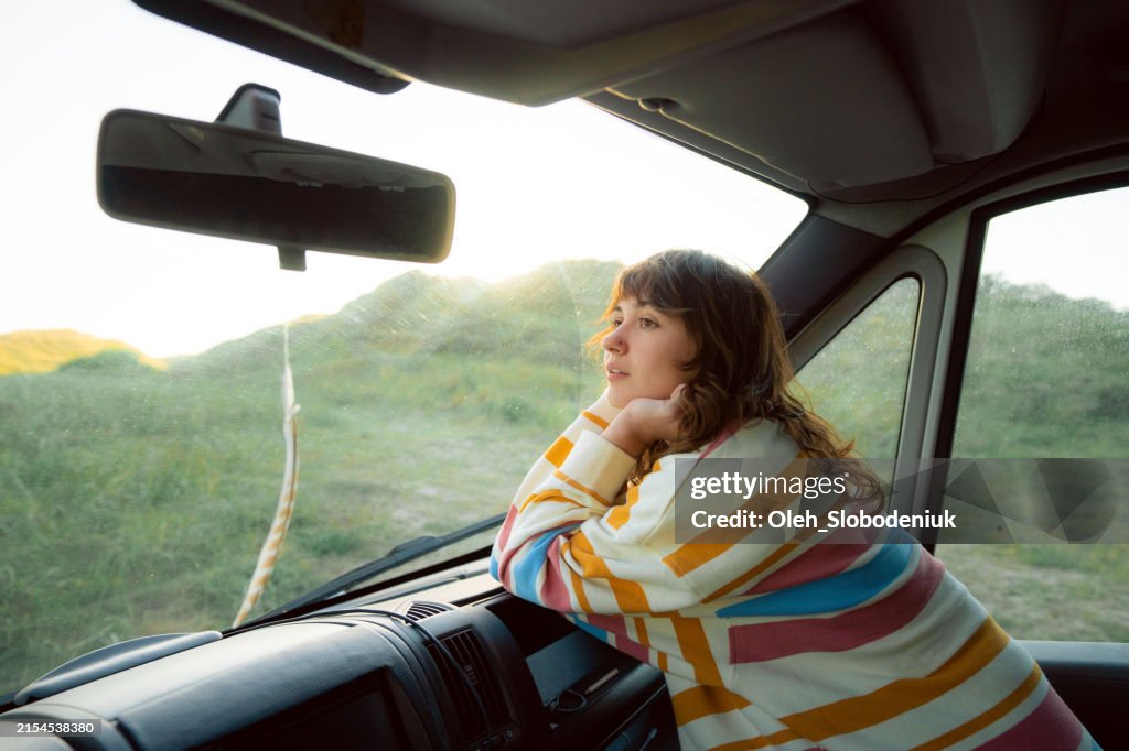 Woman in passenger seat of camper van looking through the window at Scandinavian landscape