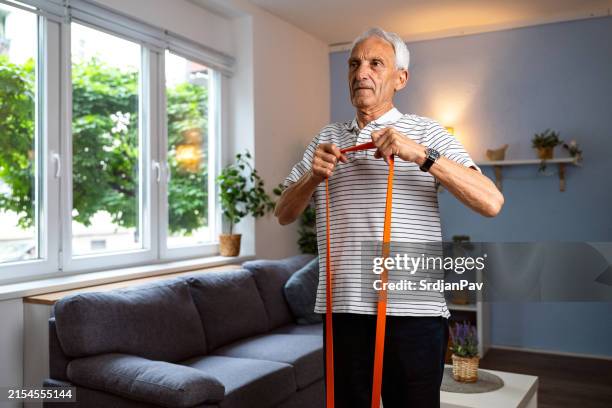 senior man exercising at home - elastiekje stockfoto's en -beelden