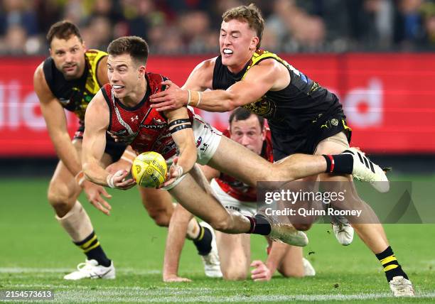 Zach Merrett of the Bombers handballs whilst being tackled by Kane McAuliffe of the Tigers during the round 11 AFL match between Richmond Tigers and...