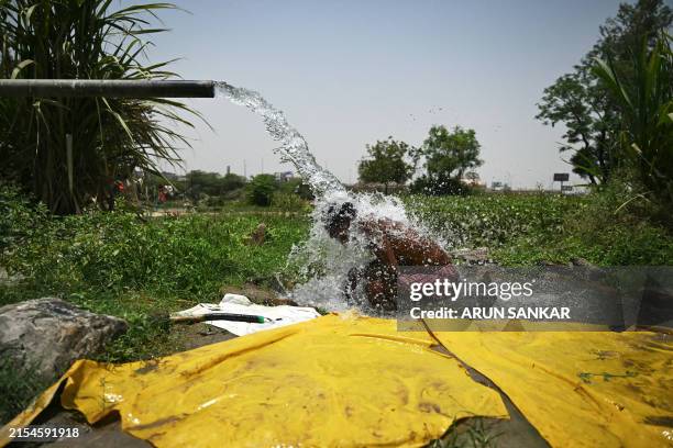 Man takes a shower under water pouring from a pipe along the Yamuna flood plains on a hot summer afternoon in New Delhi on May 29 amid ongoing...