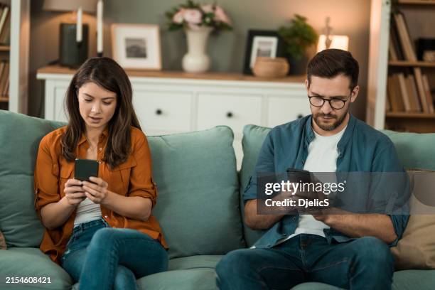 coppia che usa i telefoni sul divano. - indifferenza foto e immagini stock