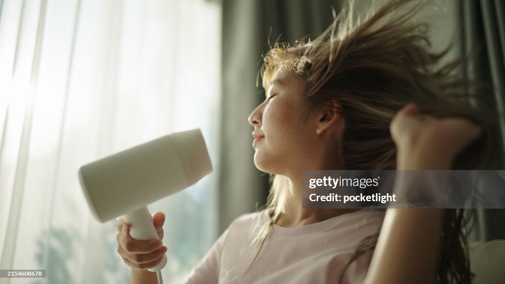 Young woman blow drying hair.