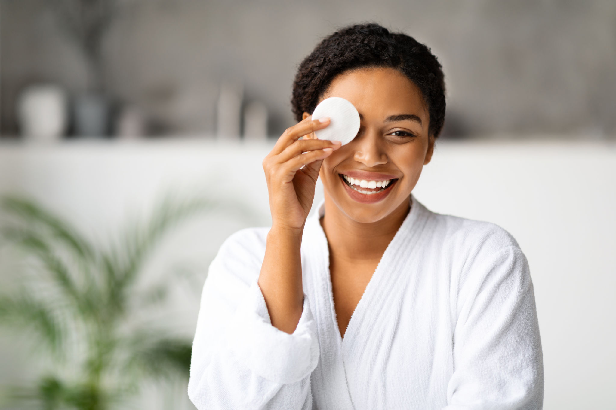 Joyful black woman removing makeup, covering eye with cotton pad Joyful black woman removing makeup, covering eye with cotton pad