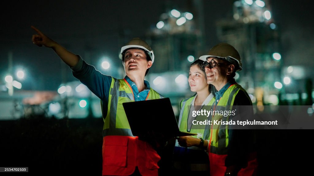Three asian Inspection engineers working with laptop of gas refinery plant and refinery oil factory industry at night .