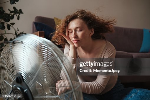 Carefree woman relaxing near electric fan at home, cooling down refreshing during heatwave indoors. Summer heat Carefree woman relaxing near electric fan at home, cooling down refreshing during heatwave indoors. Summer heat