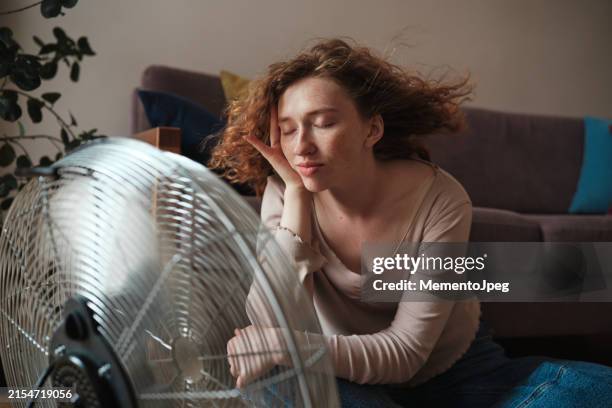 carefree woman relaxing near electric fan at home, cooling down refreshing during heatwave indoors. summer heat - feber bildbanksfoton och bilder