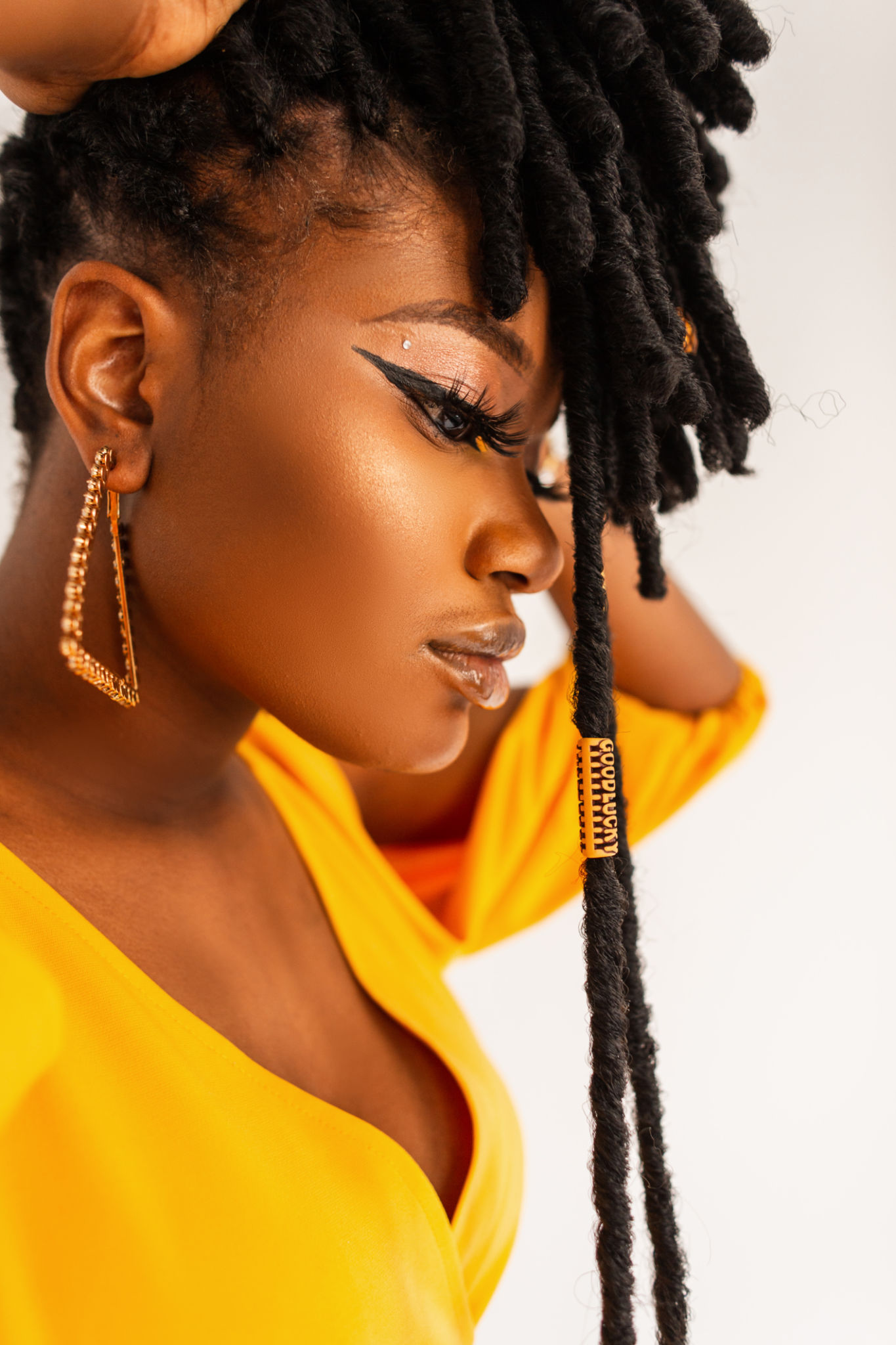 Fashion portrait of model beautiful African woman with clean healthy skin with with gold jewelry earrings with fashionable hairstyle dreadlocks in yellow dress on white background in studio. Fashion portrait of model beautiful African woman with clean healthy skin with with gold jewelry earrings with fashionable hairstyle dreadlocks in yellow dress on white background in studio.