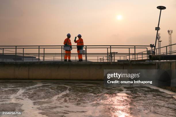 safety and environmental engineers working on the sunlight at a wastewater treatment plant in the industrial estate by walking around and checking the quality of the water - estação de tratamento de esgotos imagens e fotografias de stock
