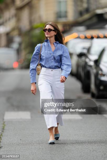 Segolene Hyppolite wears sunglasses, a blue and white oversized shirt from Tommy Hilfiger, a raffia beige bag from Vanessa Bruno, high waist white...