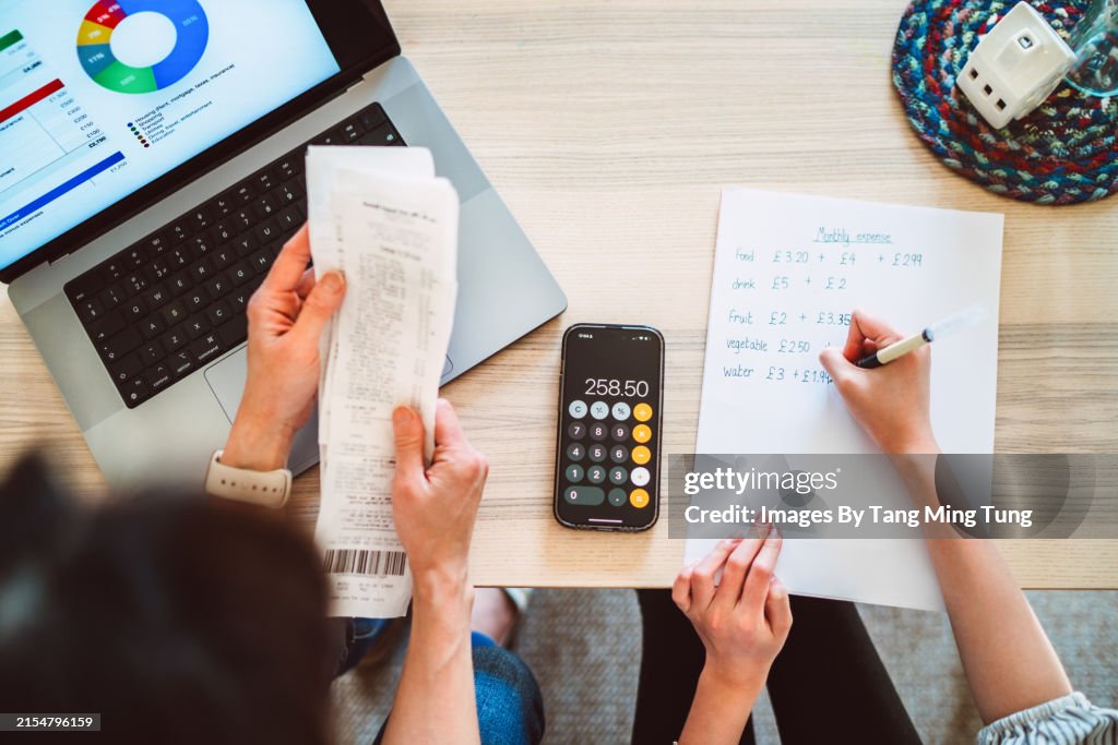 A direct above and personal perspective shot of mother and daughter managing home budget at home with the aid of A.I. financial app at home.