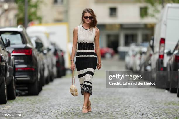 Segolene Hyppolite wears sunglasses, a sleeveless black and white embroidered wool midi dress from Vanessa Bruno, a beige raffia bag from Vanessa...