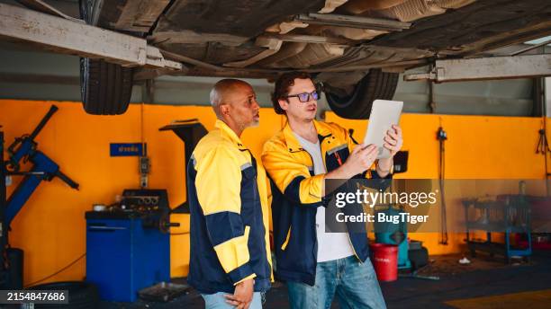 mechanic working together at auto repair shop checking under car. - brake stock pictures, royalty-free photos & images