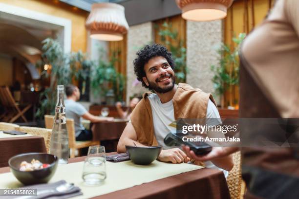 junger mann, der für das essen im restaurant bezahlt. - bankkarte stock-fotos und bilder