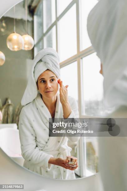 fresh-faced beauty: smiling woman applies toner in bright white bathroom - retinol stock pictures, royalty-free photos & images
