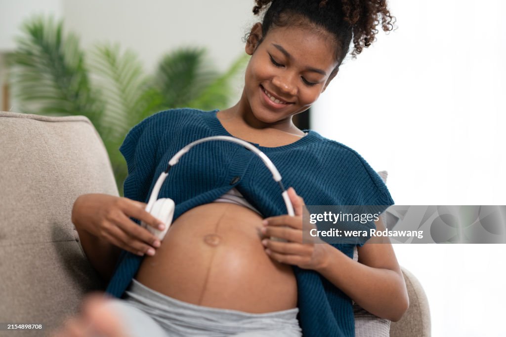 Happy pregnant woman touching headphone on the womb for the baby listen to music