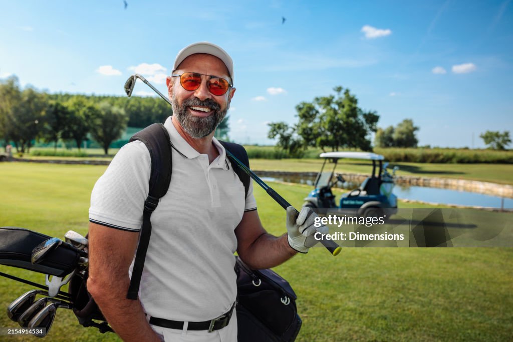 Golfeur mature heureux debout sur le terrain et souriant à la caméra