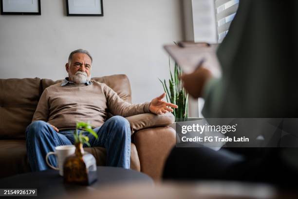 senior man talking with pshychotherapist during therapy session at clinic - post traumatic stress disorder stock pictures, royalty-free photos & images