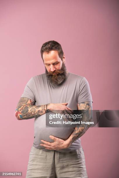 portrait of handsome man feeling discomfort and fullness in stomach, bloating. sympathetic pregnancy or couvade syndrome, partner of pregnant woman feeling similar symptoms. - bloating stock pictures, royalty-free photos & images