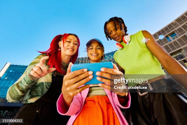 tres amigos de la generación z usando un teléfono inteligente juntos. toma de ángulo bajo con edificios modernos en el fondo. concepto de redes sociales y amistad. - gran angular fotografías e imágenes de stock