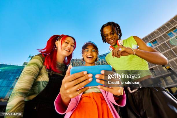 three gen z friends using a smartphone together. low angle shot with modern buildings in the background. social media and friendship concept. - low angle view stock pictures, royalty-free photos & images