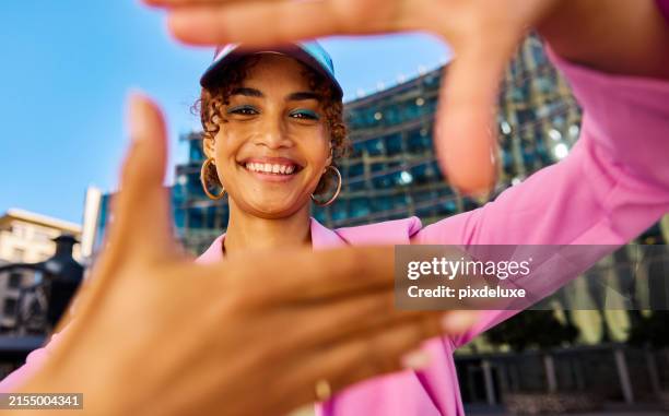 gen z woman framing her face with her hands and smiling. close-up shot with modern building in the background. positive emotions and urban lifestyle concept. - jeugdcultuur stockfoto's en -beelden