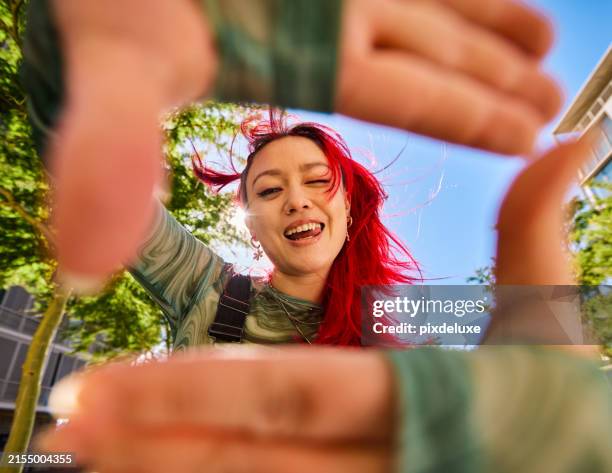 gen z adult with red hair smiling and looking through a hand frame gesture outdoors in an urban environment. low angle shot. - lente olho de peixe imagens e fotografias de stock