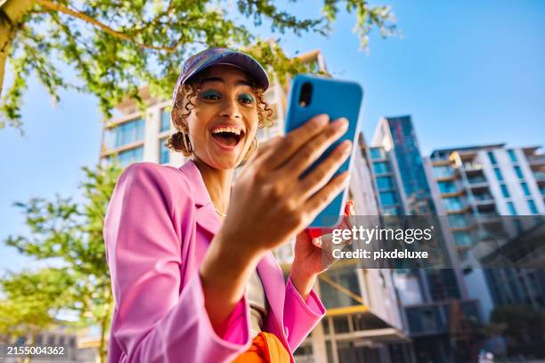 gen z adult with a cap smiling and looking at a smartphone outdoors in an urban environment. low angle shot. - keps bildbanksfoton och bilder