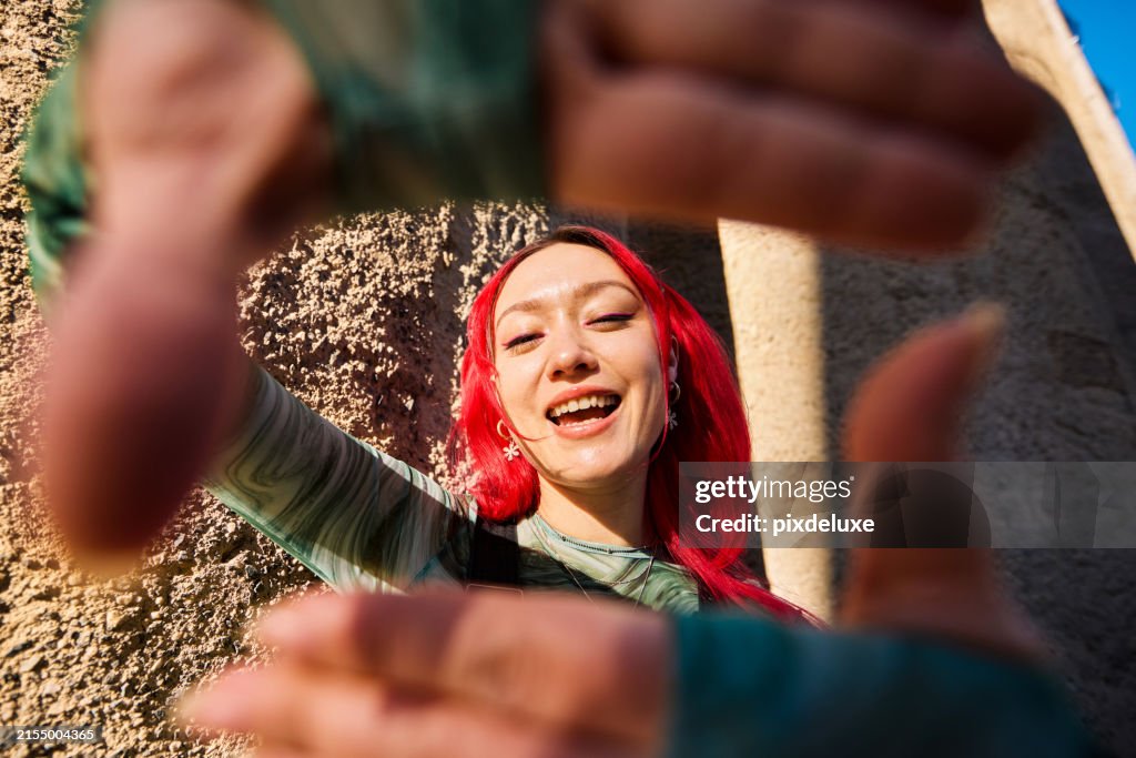 Eine Frau der Generation Z, die ihr Gesicht mit ihren Händen umrahmt und lächelt. Nahaufnahme mit modernem Gebäude im Hintergrund. Positive Emotionen und urbanes Lifestyle-Konzept.