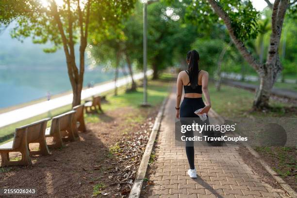 female runner stretching legs before doing her summer workout. woman warming up before outdoor workout with sun. young woman stretching in the park before running at the sunny - corredora de footing fotografías e imágenes de stock