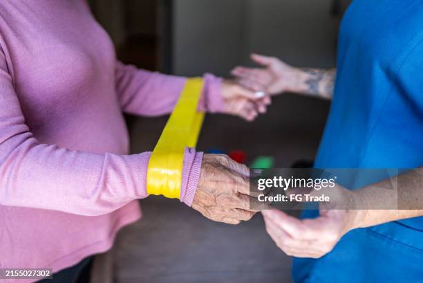 senior woman doing exercises with rubber band during house call - occupational therapy stock pictures, royalty-free photos & images