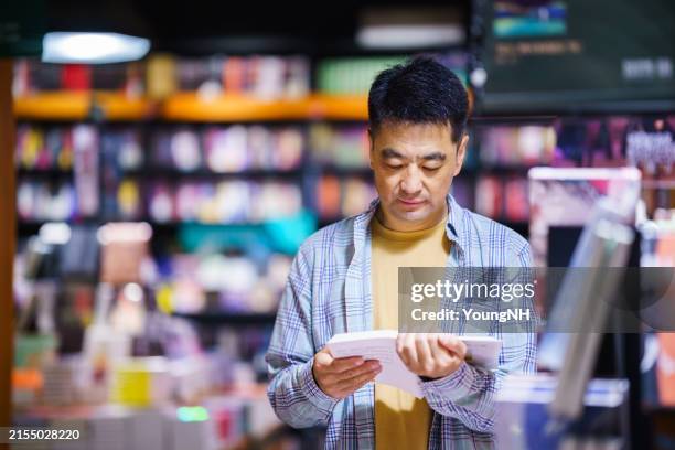 asian middle-aged man borrowing books at city public library - resource library stock pictures, royalty-free photos & images