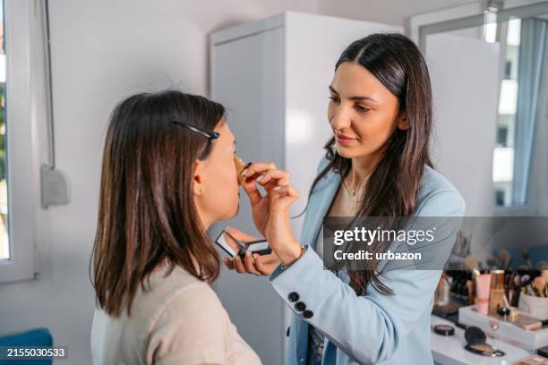 makeup artist applying compact powder foundation to her client's face with a beauty blender sponge in a beauty salon - maquilhador imagens e fotografias de stock