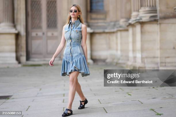 Natalia Verza wears Ray Ban sunglasses, a Balmain blue denim mini sleeveless dress with ruffles, black leather sandals from Hereu, during a street...