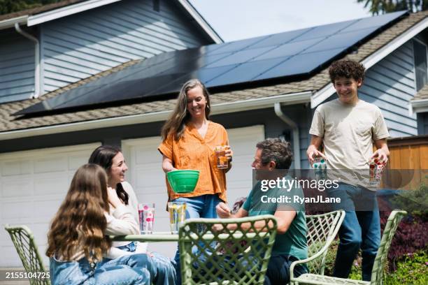 family enjoying snack outdoors in front of solar equipped home - zonnepaneel stockfoto's en -beelden