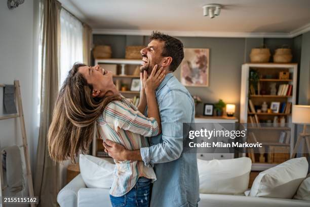 a beautiful scene of love and happiness between a couple in love enjoying their new apartment, dancing with joyful expressions in the living room - amore foto e immagini stock