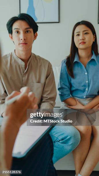 asiatische psychotherapeutin, die ein paar nach der beratung über psychische gesundheit und beziehung berät. professionelle sozialarbeiter stehen ehepaaren mit einfühlungsvermögen zur seite. vertikaler bildschirm. - eheberatung stock-fotos und bilder