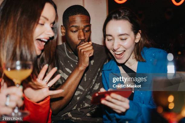 happy woman sharing smart phone with male and female friends at nightclub - vie sociale photos et images de collection