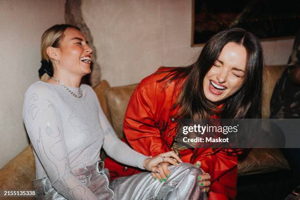 carefree female friends laughing while sitting on couch at nightclub - nightlife stock pictures, royalty-free photos & images