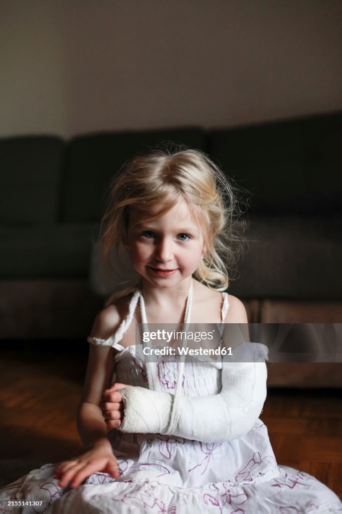 Girl with broken arm sitting on floor at home