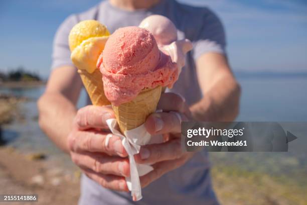 man holding colorful ice cream in waffle cups on sunny day at seashore - magenta stock pictures, royalty-free photos & images