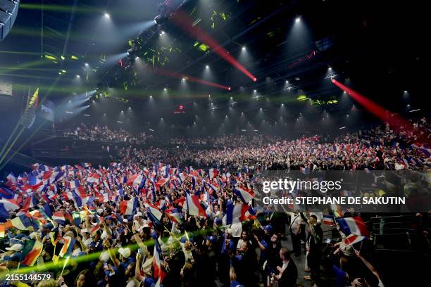 Attendees wave French flags before a campaign meeting of French far-right party Rassemblement National party's lead candidate Jordan Bardella and RN...