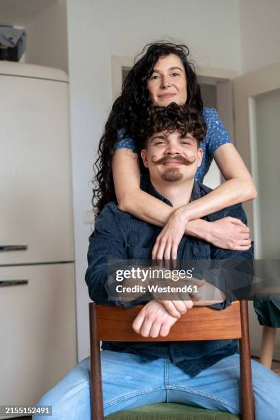 smiling woman with arms around man sitting on chair at home - hugging a chair stock pictures, royalty-free photos & images