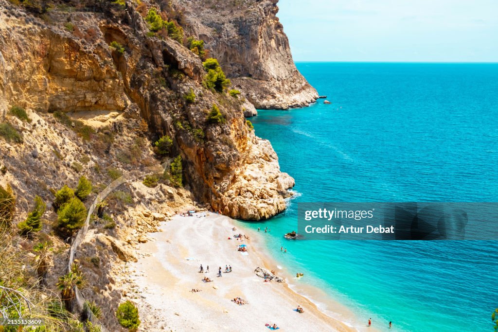 People swimming in a paradise beach with rocky terrain on the coast of the Comunidad Valenciana.