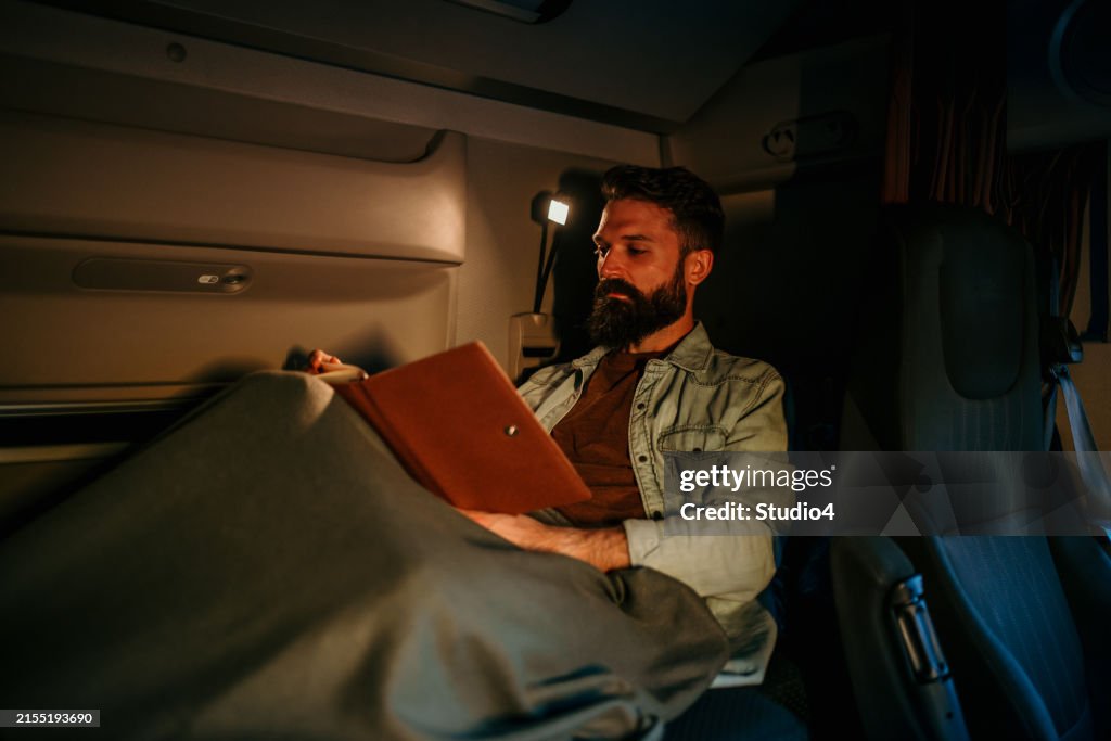 A handsome truck driver reading his book while he is taking a rest on the cabin's bed