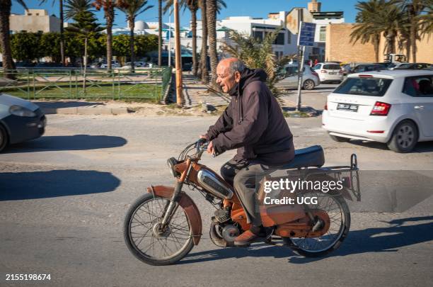 An elderly man rides a Motobecane scooter next to the Great Mosque in the medina in Mahdia, Tunisia.