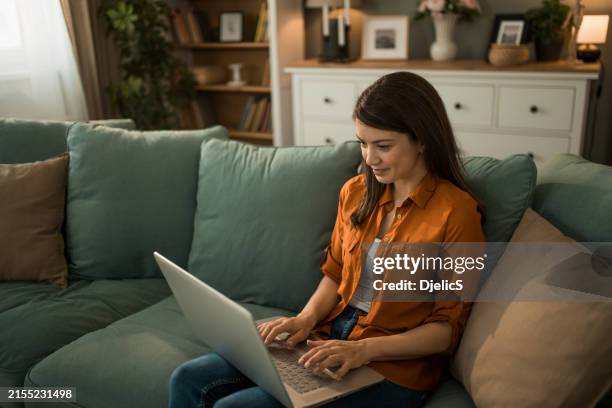 woman using laptop on sofa at home. - computer-shopping stock pictures, royalty-free photos & images