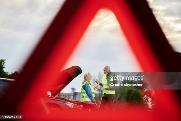pareja de ancianos discutiendo después de la falla de su automóvil en la carretera. - triángulo-de-advertencia fotografías e imágenes de stock