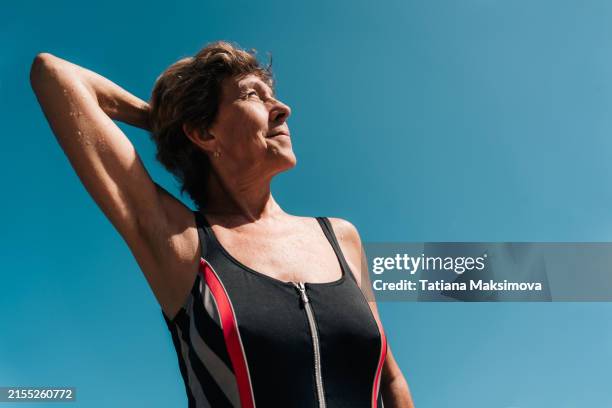 a woman of retirement age in fashionable swimsuit against the blue sky. the concept of sports swimming and active recreation on the beach. - wide angle stock pictures, royalty-free photos & images