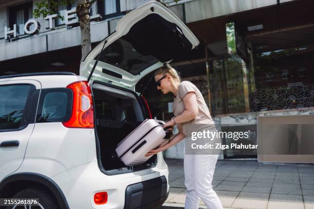woman loading suitcase into car trunk - car rental stock pictures, royalty-free photos & images
