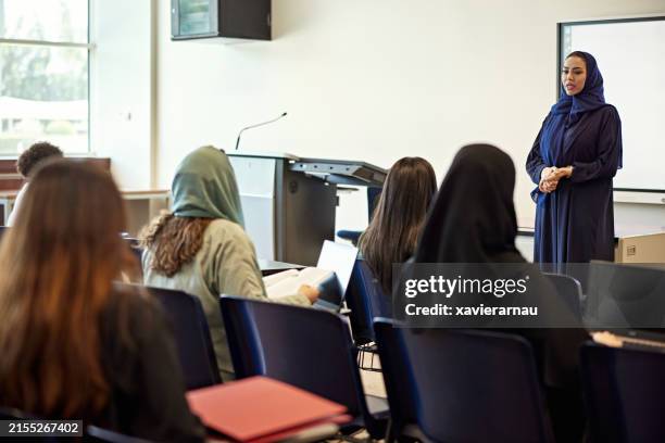 female teacher in hijab teaching group of students sitting in lecture hall at university - islamismo imagens e fotografias de stock